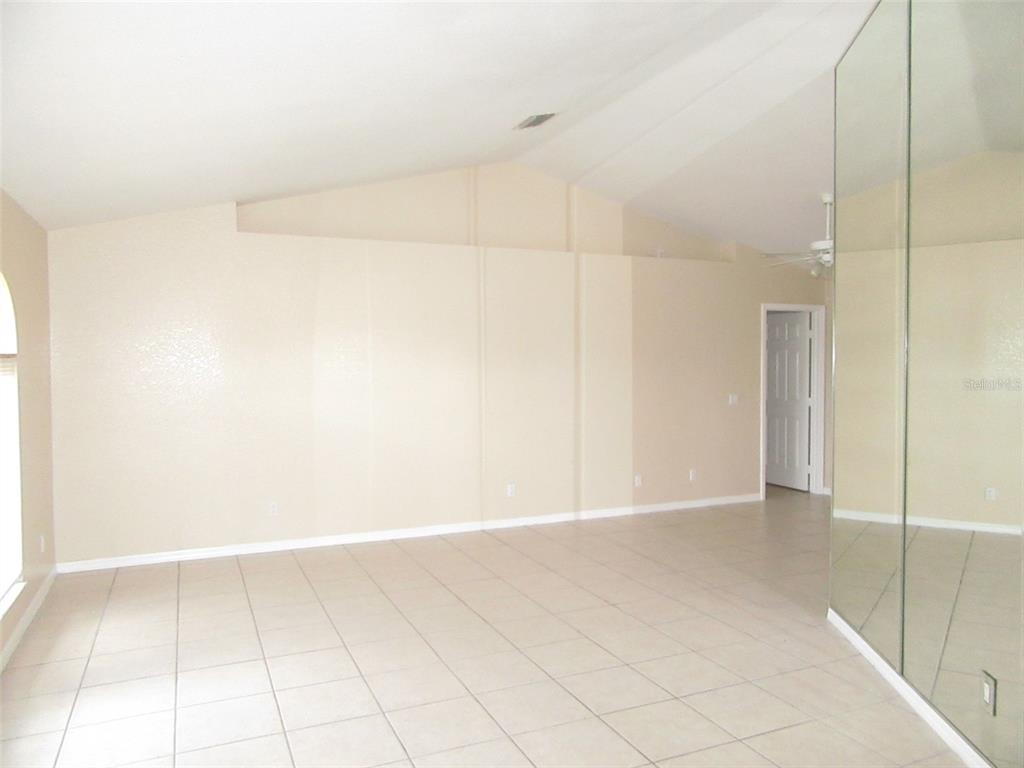 An empty room with beige walls, vaulted ceilings, tiled floors, and a mirrored wall — 22182 PEACHLAND BOULEVARD, PORT CHARLOTTE, FL