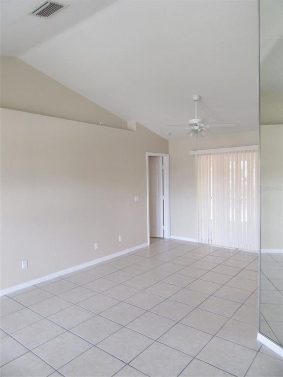 An empty room with beige walls, tile flooring, a vaulted ceiling, and a ceiling fan — 22182 PEACHLAND BOULEVARD, PORT CHARLOTTE, FL