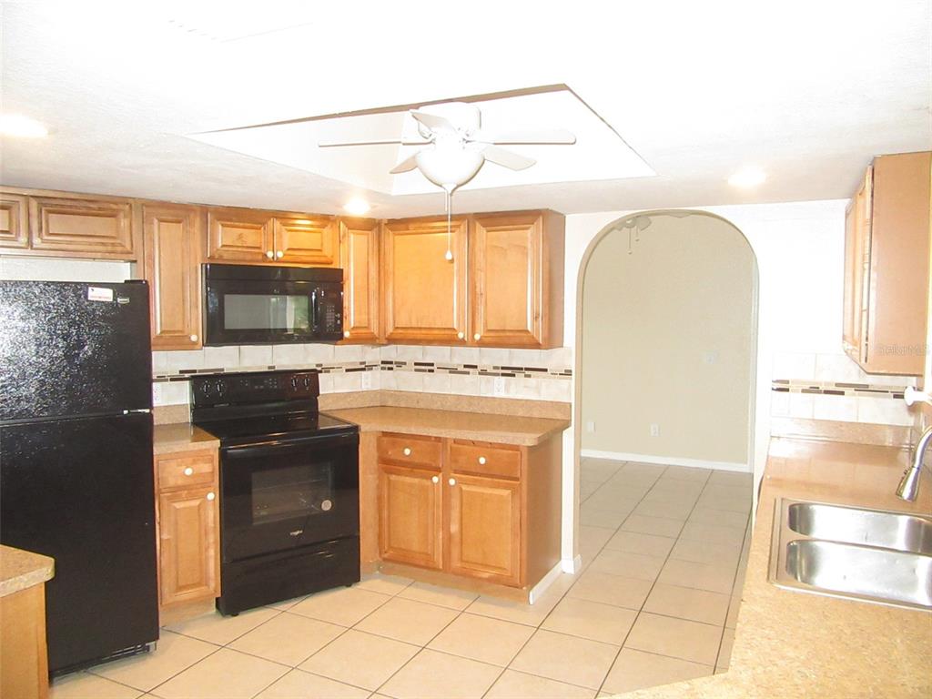 A kitchen features wood cabinets, black appliances, tile flooring, and an arched doorway — 22182 PEACHLAND BOULEVARD, PORT CHARLOTTE, FL