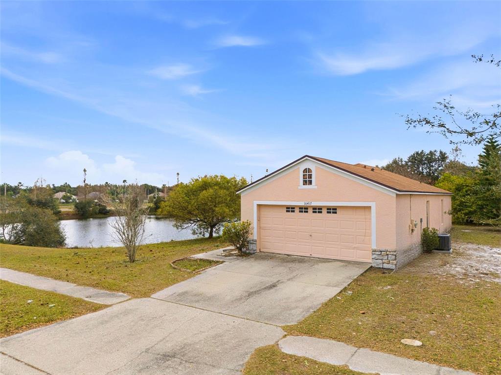 A detached, peach-colored garage with a concrete driveway sits next to a small lake — 10417 BLACKMORE DRIVE, TAMPA, FL