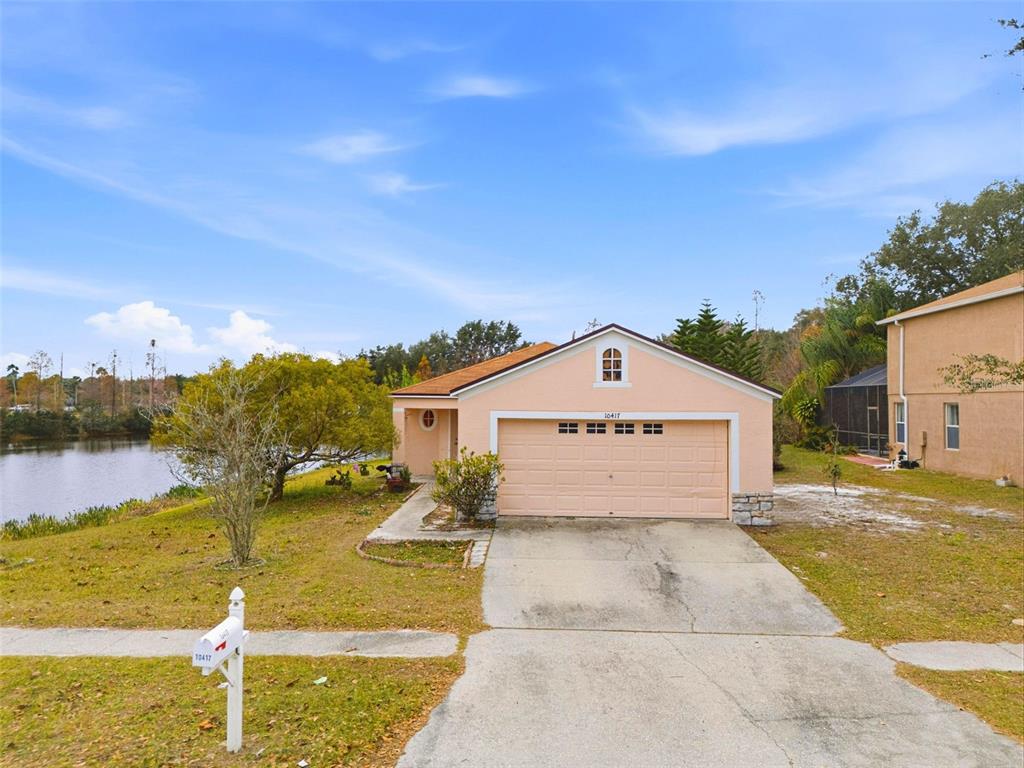 A single-story peach-colored house with a two-car garage sits next to a lake — 10417 BLACKMORE DRIVE, TAMPA, FL
