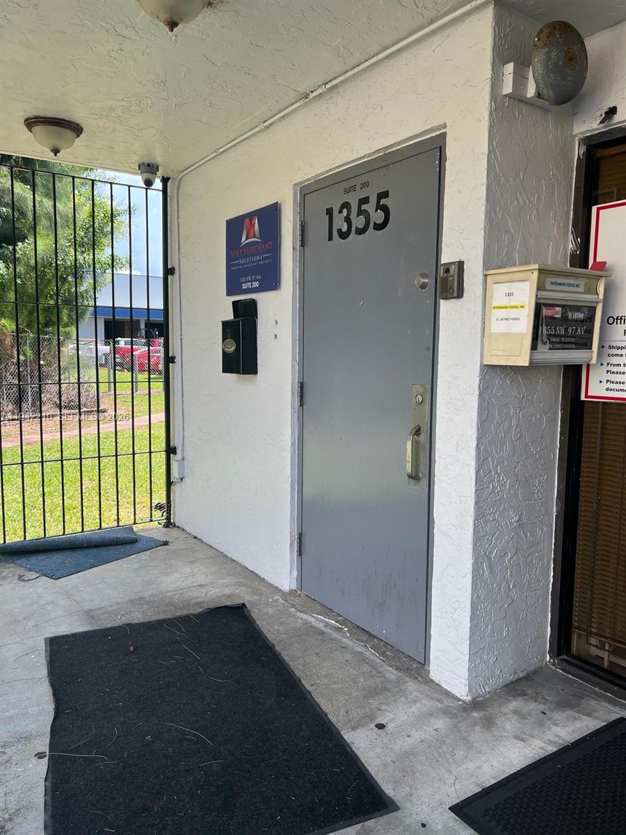 An exterior view of a commercial building entrance with a gray door labeled 1355 — 1355 NW 97 Avenue, Doral FL 33172, DORAL, FL