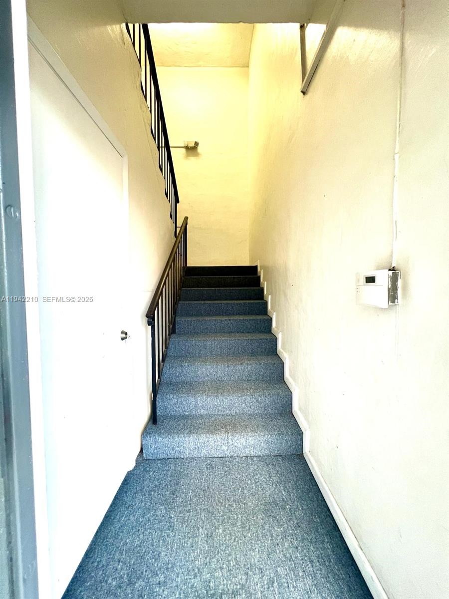 A carpeted staircase with a black metal railing leads upward between two white walls — 1355 NW 97 Avenue, Doral FL 33172, DORAL, FL