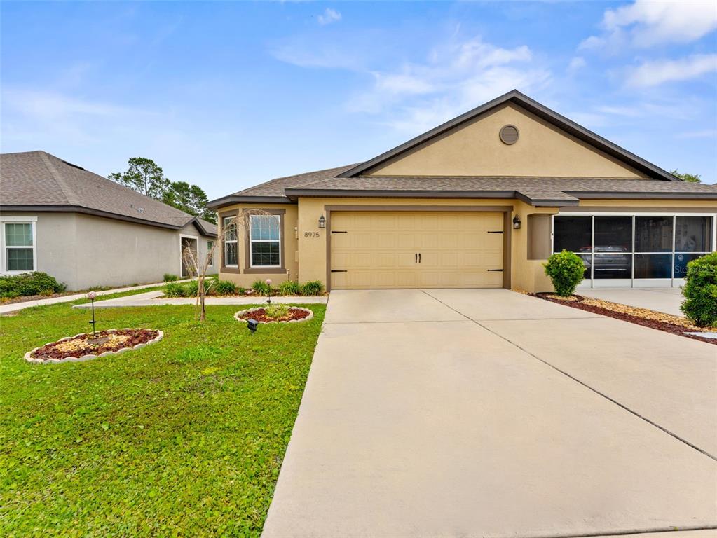 A tan single-story house features a two-car garage, a concrete driveway, and a small lawn — 8975 SOUTHERN CHARM CIRCLE, BROOKSVILLE, FL