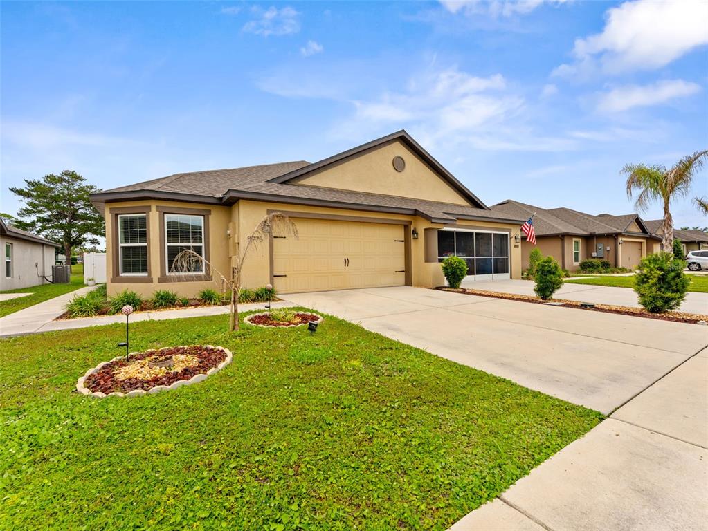 A tan single-story house with a two-car garage and a landscaped front yard — 8975 SOUTHERN CHARM CIRCLE, BROOKSVILLE, FL