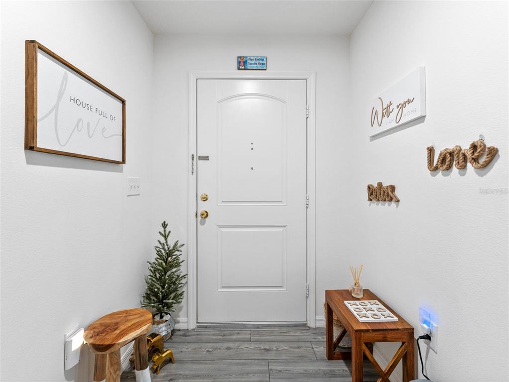 An entryway features a white door, wood-look flooring, decorative wall signs, and a small bench — 8975 SOUTHERN CHARM CIRCLE, BROOKSVILLE, FL
