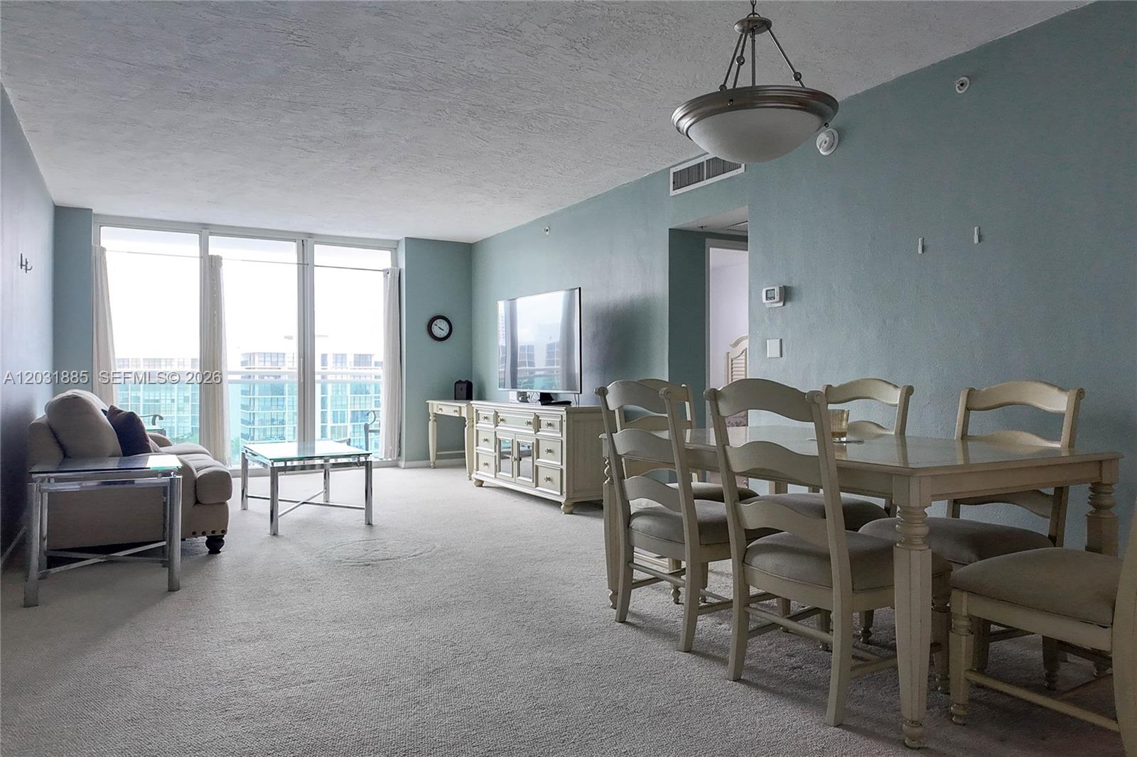 A living and dining area features light blue walls, carpeted floors, and a balcony view — 3000 S Ocean Dr # 712, Hollywood FL 33019, HOLLYWOOD, FL
