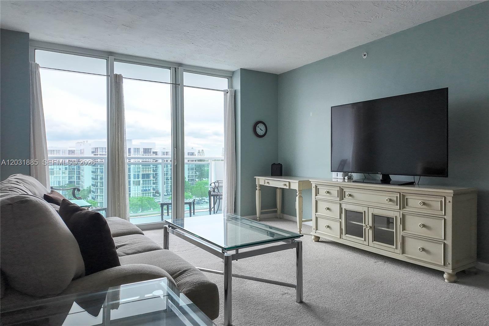 A living room features a beige sofa, glass coffee table, media console, and balcony access — 3000 S Ocean Dr # 712, Hollywood FL 33019, HOLLYWOOD, FL