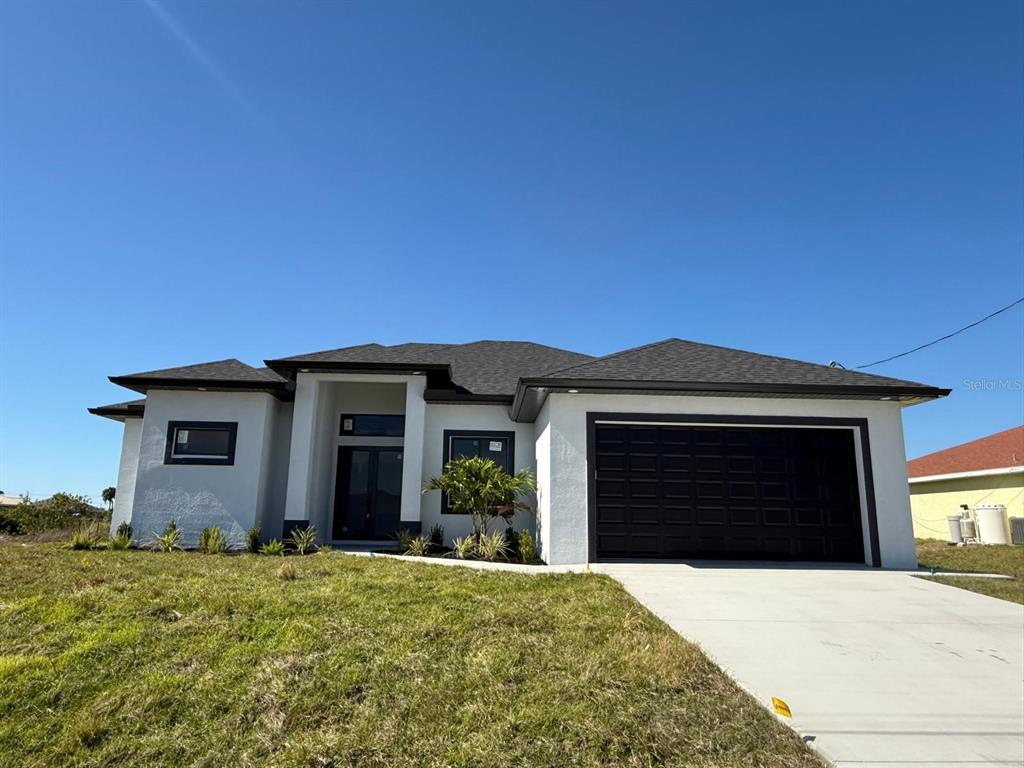A modern, single-story house with white stucco walls, a dark garage door, and a hip roof — 1320 NE 14TH AVENUE, CAPE CORAL, FL