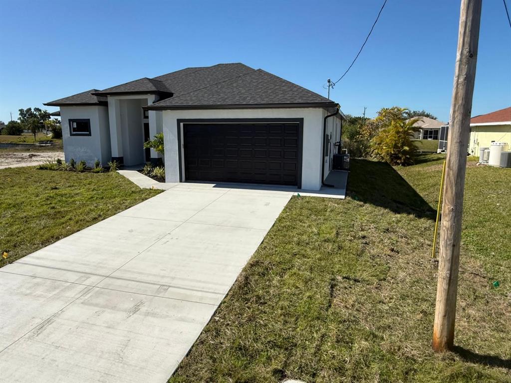 A modern, single-story house with a dark garage door, white stucco walls, and a concrete driveway — 1320 NE 14TH AVENUE, CAPE CORAL, FL