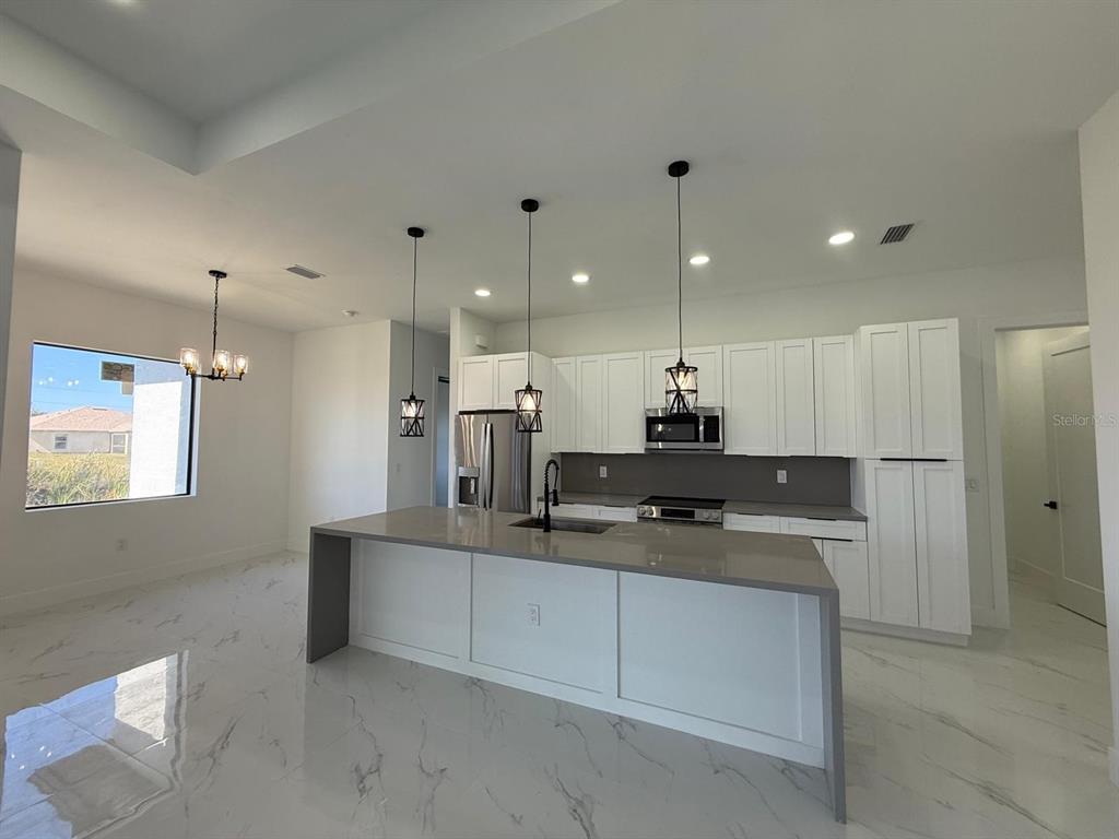 A modern kitchen features white cabinetry, a large gray island, and marble-look tile flooring — 1320 NE 14TH AVENUE, CAPE CORAL, FL