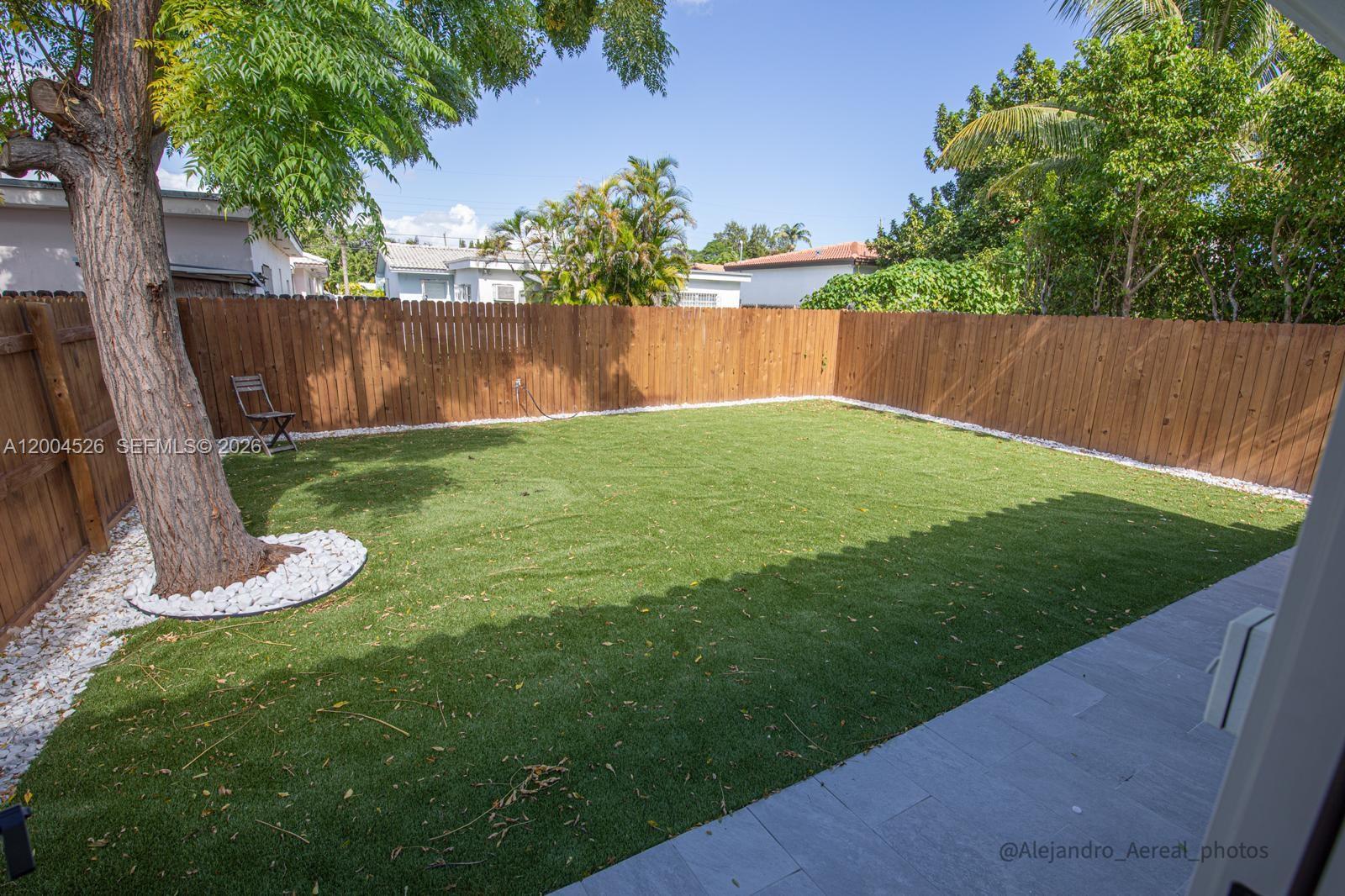 A fenced backyard features artificial turf, a large tree, and a stone-tiled patio area — 3045 SW 21st St, Miami FL 33145, MIAMI, FL