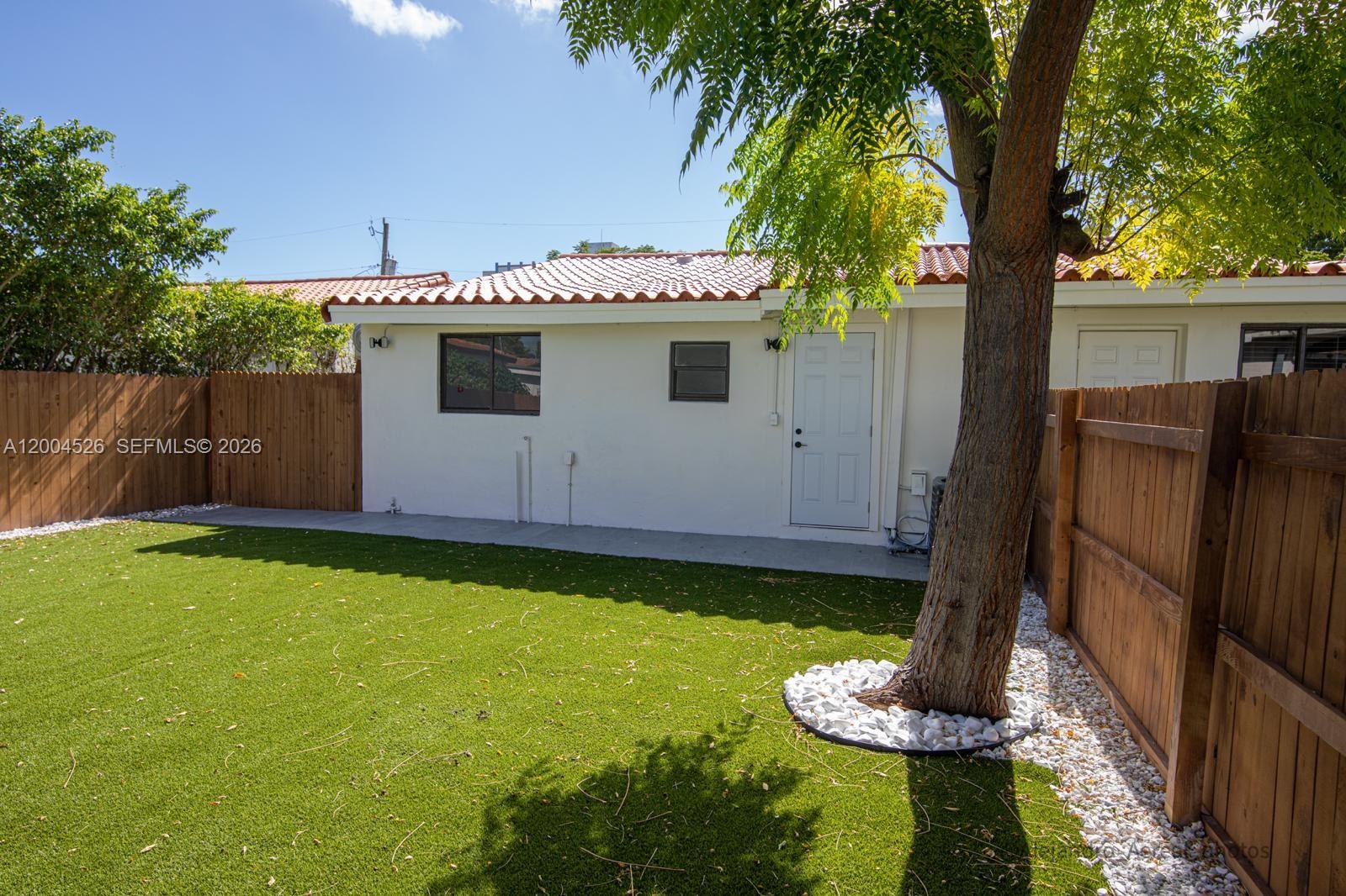 A backyard features artificial turf, a white stucco building with a tiled roof, and a tree — 3045 SW 21st St, Miami FL 33145, MIAMI, FL