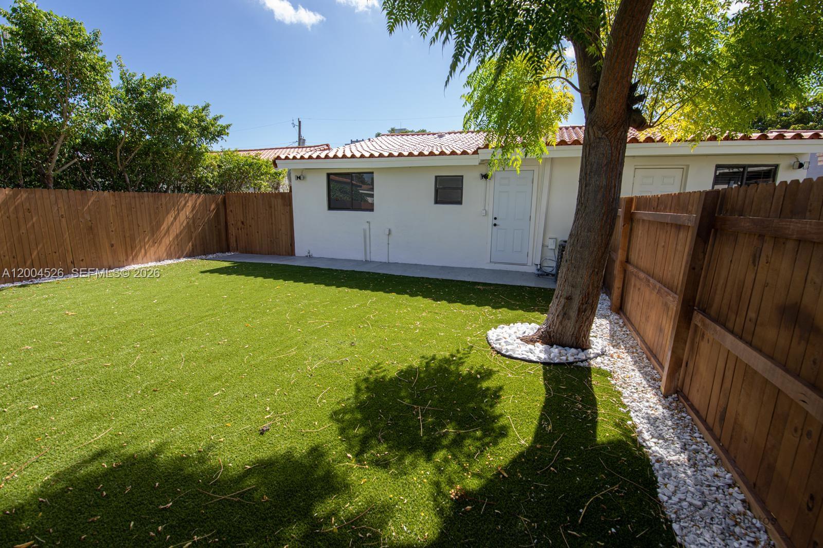 A backyard features artificial turf, a wooden fence, and a tree with white decorative stones — 3045 SW 21st St, Miami FL 33145, MIAMI, FL