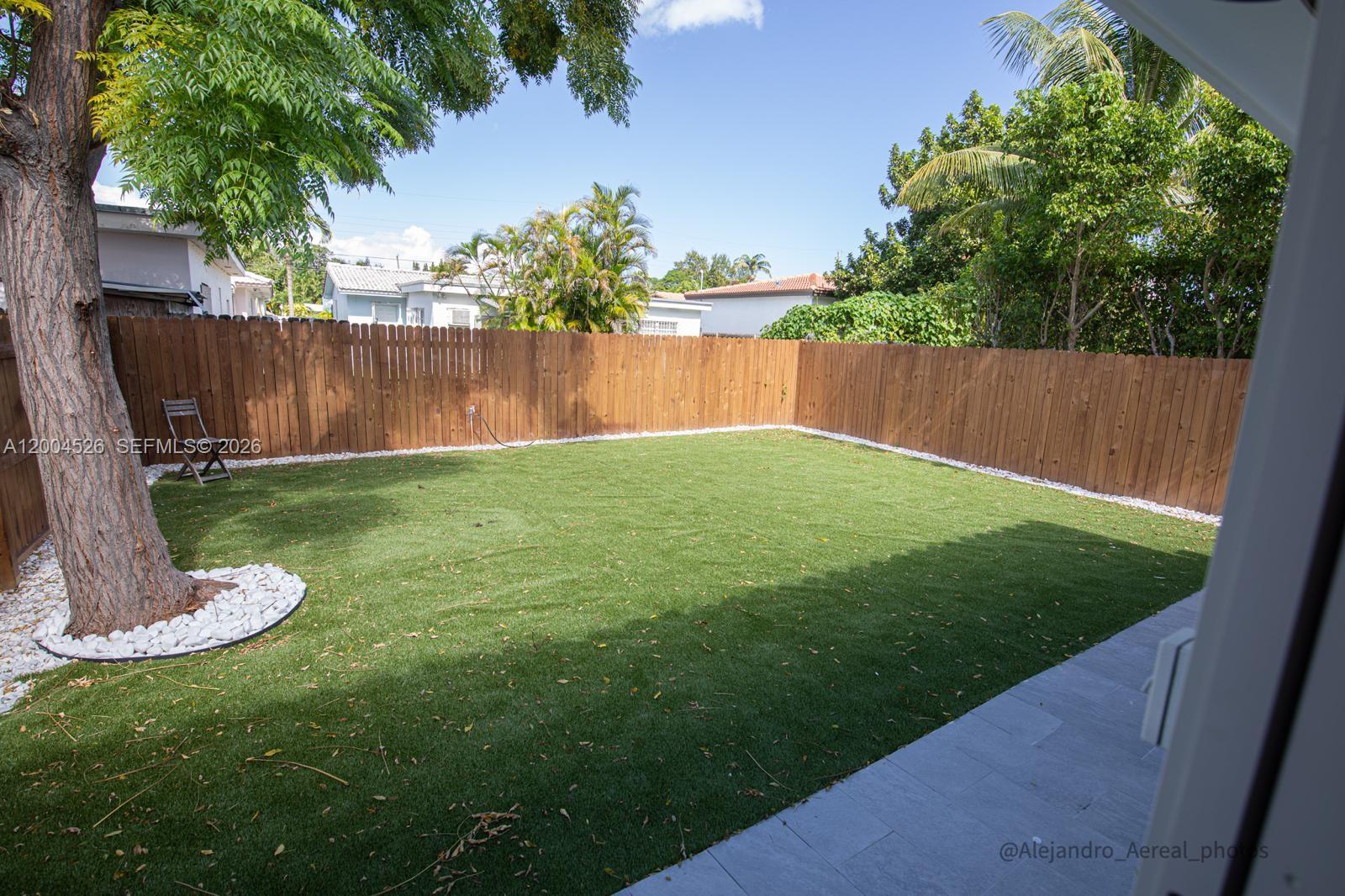 A fenced backyard features artificial turf, a large tree, and a stone-bordered garden bed — 3045 SW 21st St, Miami FL 33145, MIAMI, FL