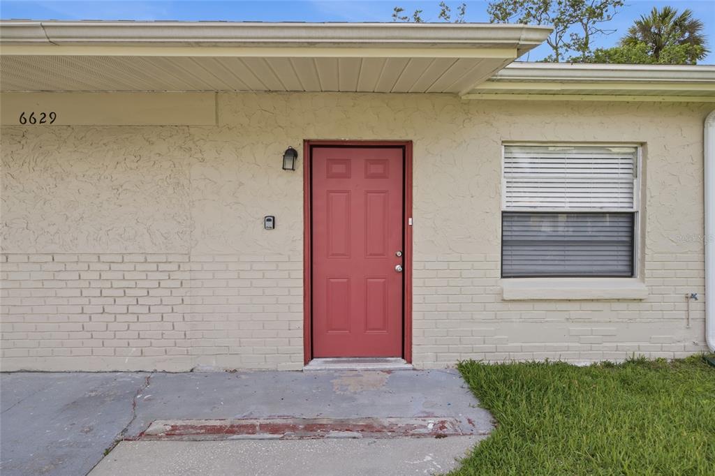 The exterior of a single-story home features a red front door and a brick facade — 6629 SIERRA TERRACE, NEW PORT RICHEY, FL