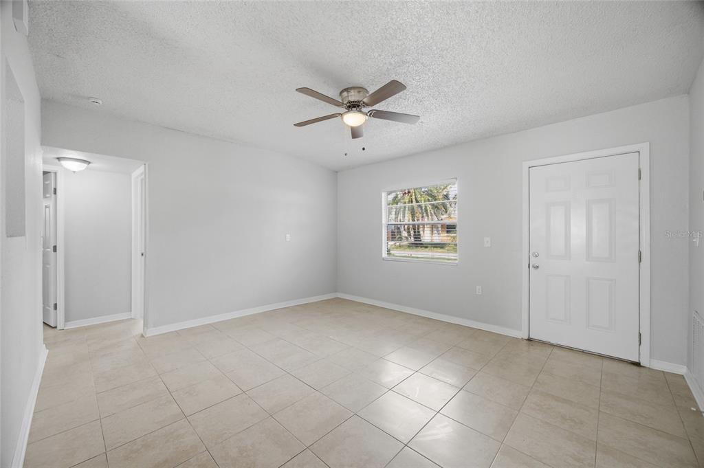 An empty room with light-colored tile flooring, a ceiling fan, and a white entry door — 6629 SIERRA TERRACE, NEW PORT RICHEY, FL