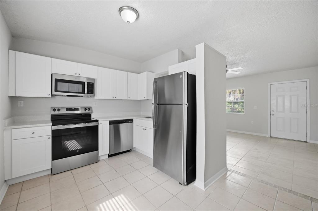 A kitchen with white cabinets, stainless steel appliances, and tile flooring opens to a living area — 6629 SIERRA TERRACE, NEW PORT RICHEY, FL