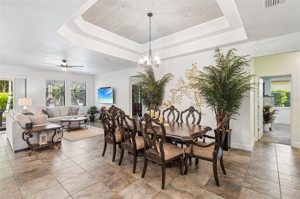 A dining area with a tray ceiling and chandelier sits adjacent to a living room — 4586 GRAND LAKESIDE DRIVE, PALM HARBOR, FL