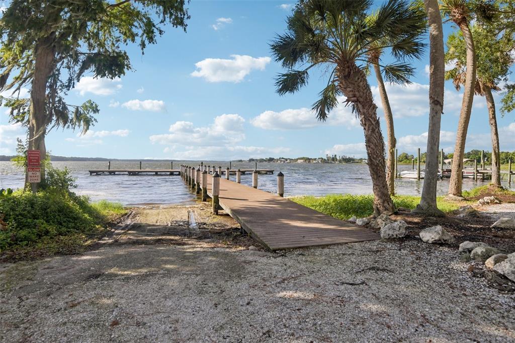 A wooden dock extends into a lake from a gravel boat ramp near palm trees — 4586 GRAND LAKESIDE DRIVE, PALM HARBOR, FL