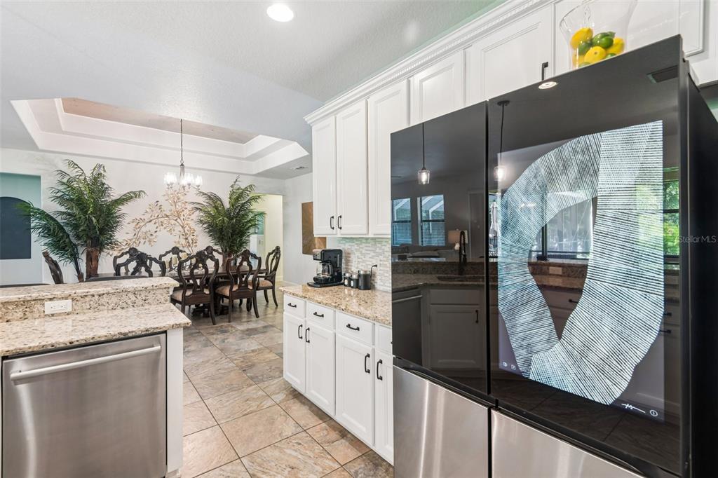A kitchen with white cabinets, granite countertops, and a smart refrigerator next to a dining area — 4586 GRAND LAKESIDE DRIVE, PALM HARBOR, FL