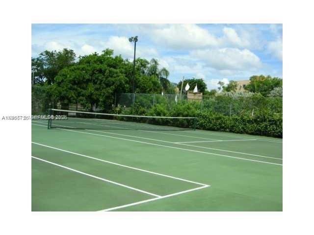 A green tennis court with a net is surrounded by a chain-link fence and trees — 18330 NW 68th Ave # A, Hialeah FL 33015, HIALEAH, FL