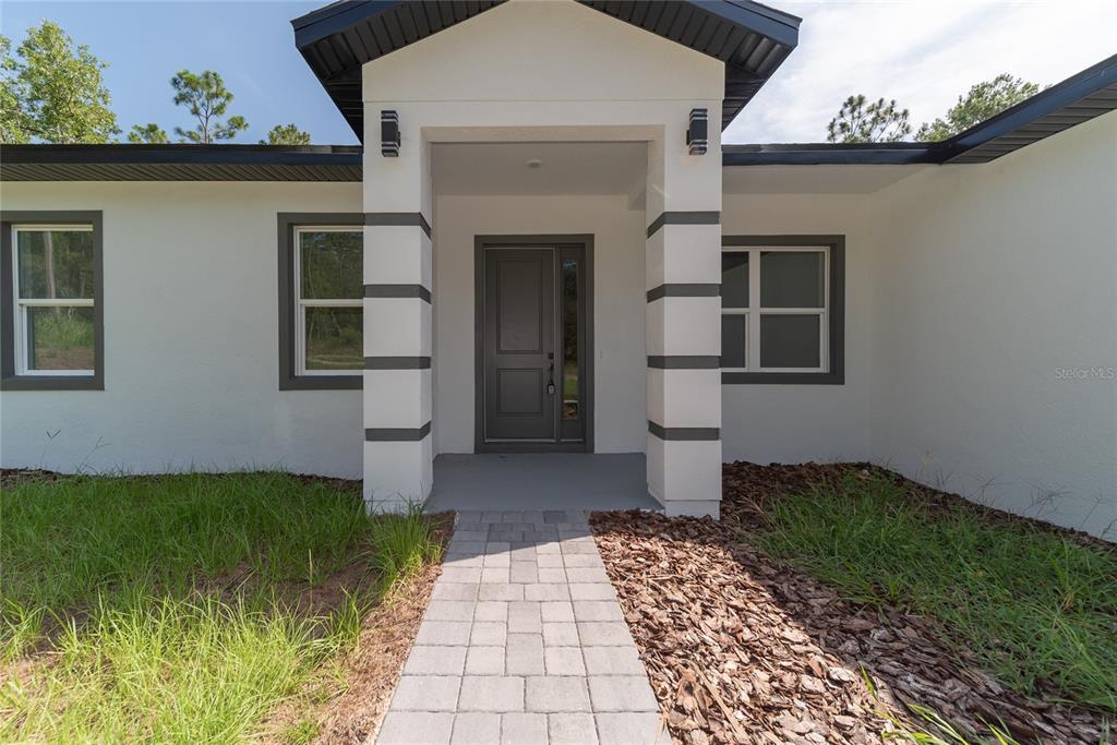 The exterior of a modern house features a white facade, dark trim, and a paved walkway — 3691 W NORWICK PLACE, DUNNELLON, FL