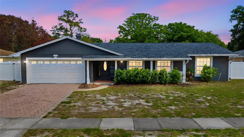 A single-story house with a dark gray exterior, white garage door, and a brick driveway — 8509 SANDBERRY BOULEVARD, ORLANDO, FL