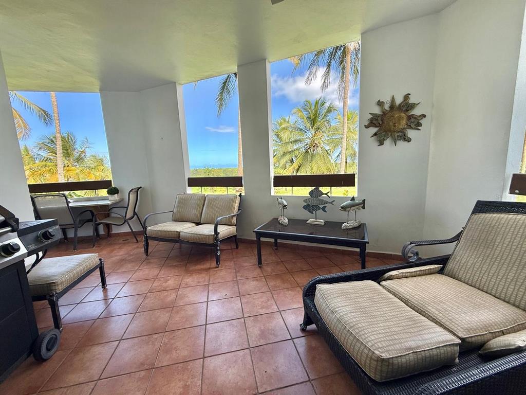 A covered outdoor patio features tile flooring, patio furniture, and views of palm trees and ocean — 3801 RIO MAR VILLAGE, RIO GRANDE, PR