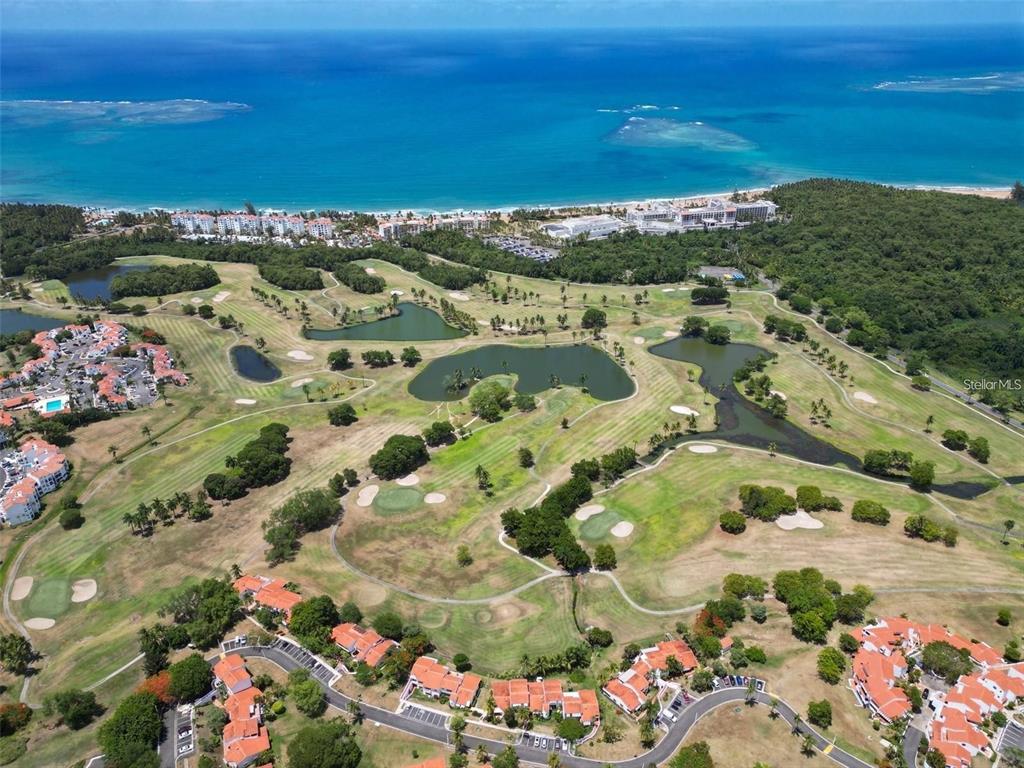 An aerial view shows a golf course with several ponds surrounded by residential buildings and ocean — 3801 RIO MAR VILLAGE, RIO GRANDE, PR