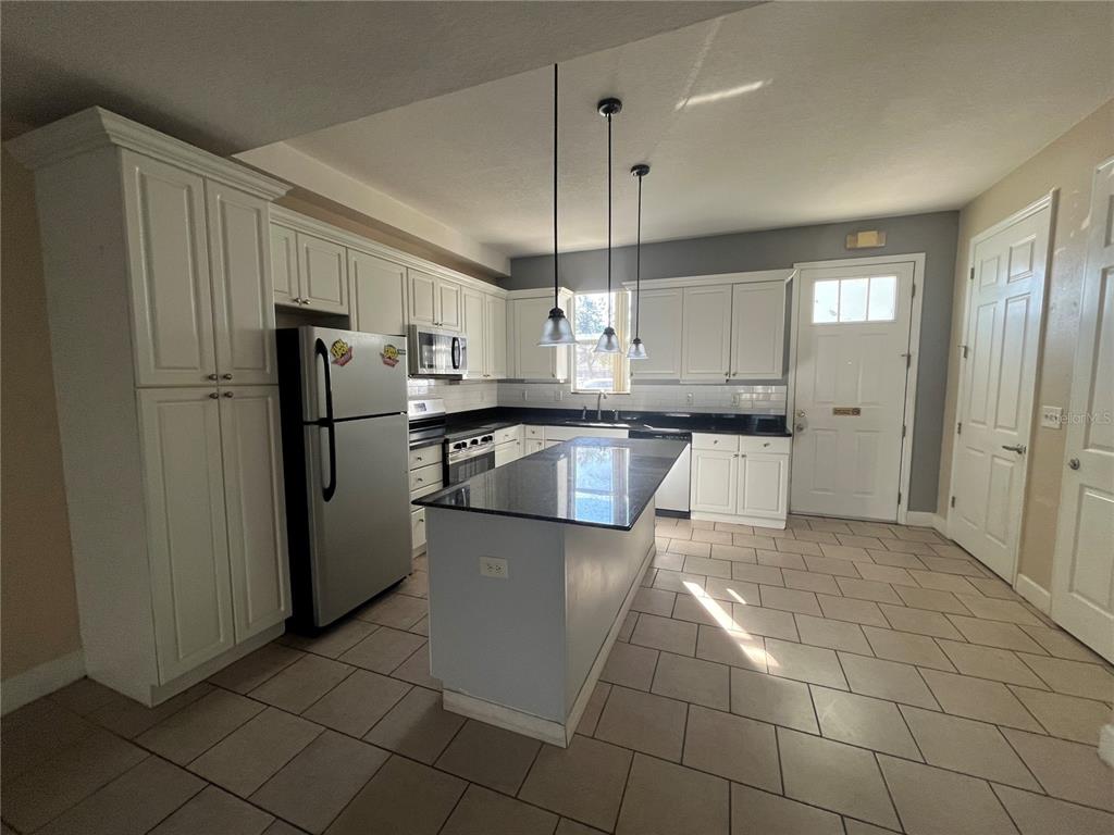 A kitchen features white cabinets, stainless steel appliances, a dark island, and light tile flooring — 2013 GRAND OAK DRIVE, KISSIMMEE, FL