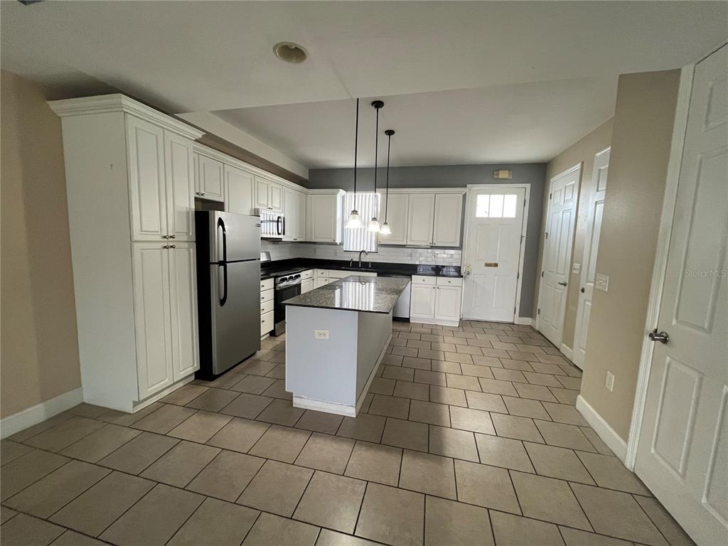 A kitchen features white cabinetry, a granite-topped island, stainless steel appliances, and tile flooring — 2013 GRAND OAK DRIVE, KISSIMMEE, FL