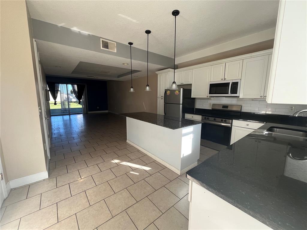 A kitchen features white cabinets, dark granite countertops, stainless steel appliances, and tile flooring — 2013 GRAND OAK DRIVE, KISSIMMEE, FL
