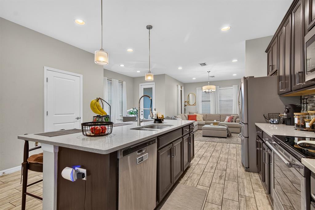A kitchen with dark cabinets, quartz countertops, and a large island overlooks an open living area — 6717 CITRUS CREEK LANE, TAMPA, FL