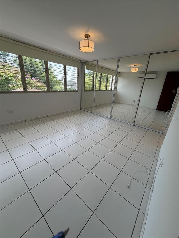 An empty room features white tiled floors, large windows, and a wall of mirrored closet doors — G7 SICILIA, GUAYNABO, PR