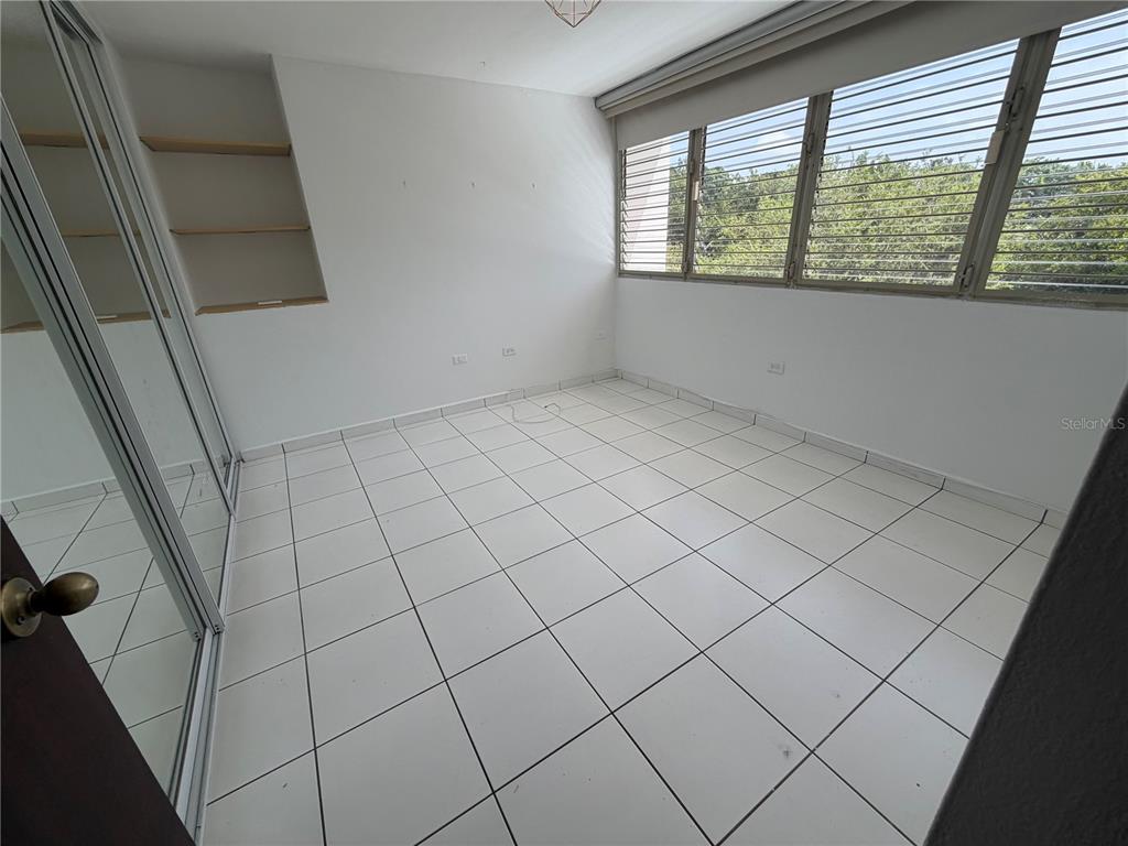 An empty bedroom features white tile flooring, a mirrored closet, and built-in wall shelving — G7 SICILIA, GUAYNABO, PR