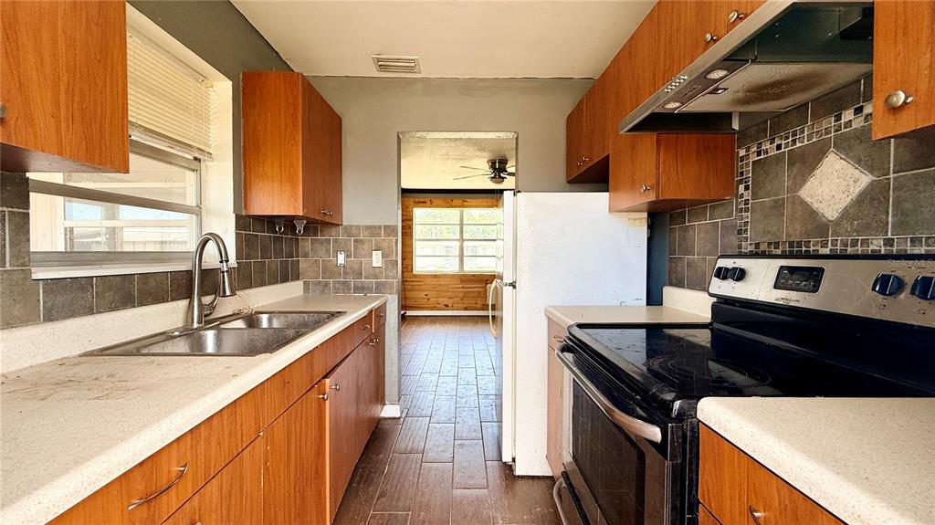 A galley kitchen features wood cabinets, dark tile backsplashes, and a black electric range — 4448 CHICOPA STREET, NORTH PORT, FL