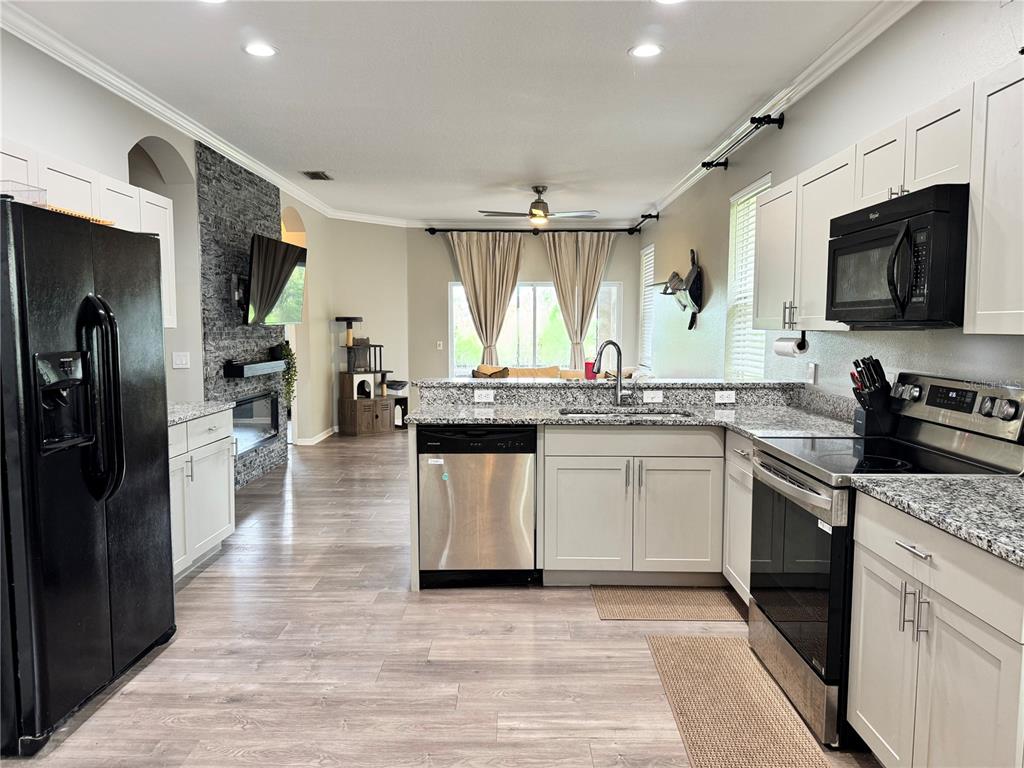 A kitchen with white cabinets, granite countertops, and stainless steel appliances overlooks a living area — 14331 GNATCATCHER TERRACE, BRADENTON, FL