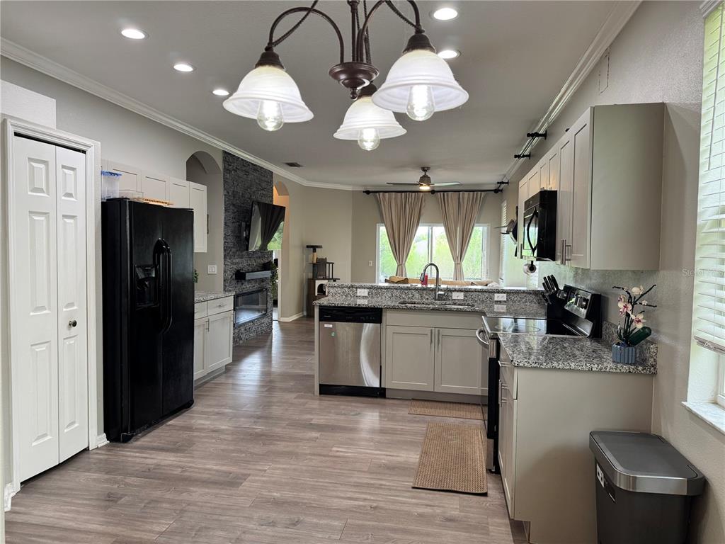 A kitchen with grey cabinets, granite countertops, stainless steel appliances, and a stone fireplace — 14331 GNATCATCHER TERRACE, BRADENTON, FL