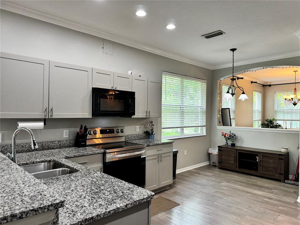A kitchen with grey cabinets, granite countertops, and stainless steel appliances opens to a living area — 14331 GNATCATCHER TERRACE, BRADENTON, FL