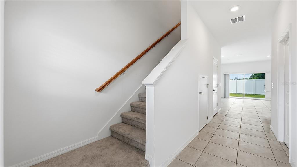 A carpeted staircase with a wooden handrail sits beside a tiled hallway leading to glass doors — 4790 REVOLUTIONARY WAY, ST CLOUD, FL
