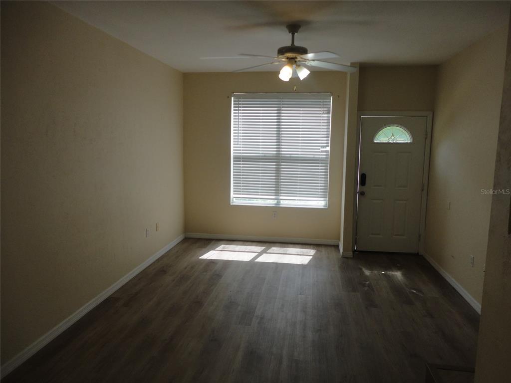 An empty room features light-colored walls, wood-look flooring, a ceiling fan, and a front door — 3584 SW 30TH WAY UNIT 129, GAINESVILLE, FL