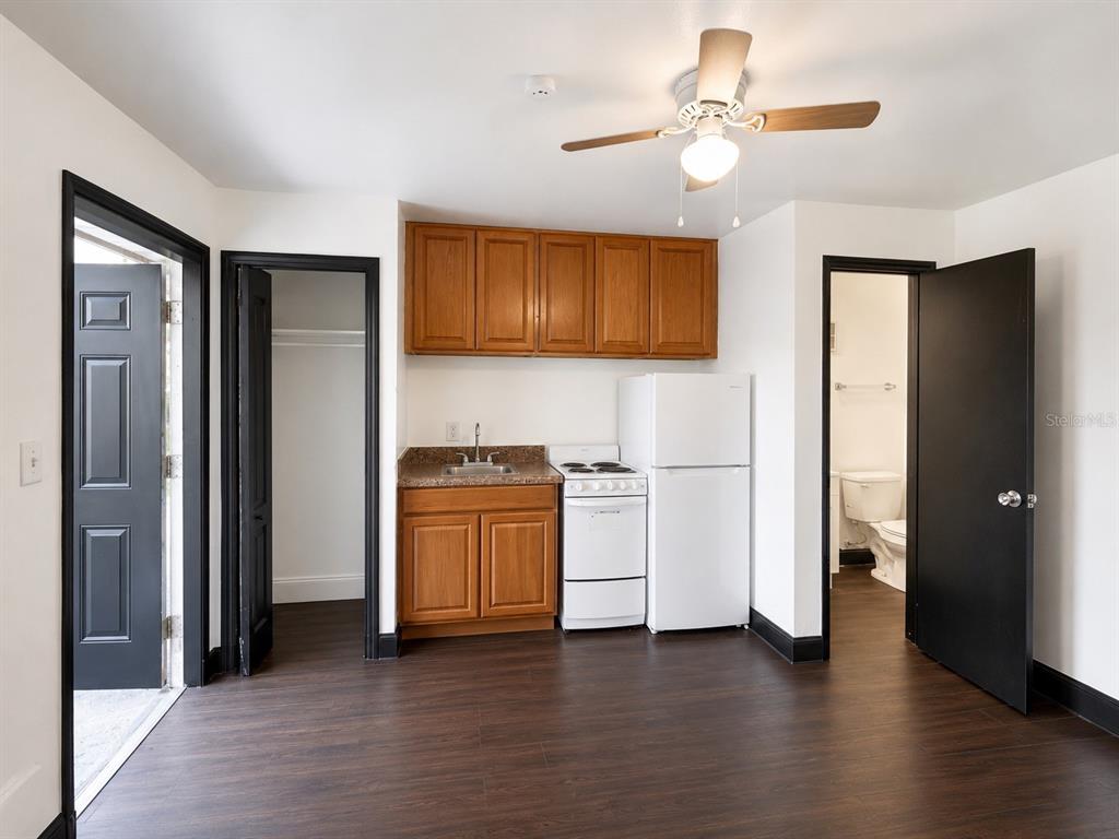 A small kitchen area features wooden cabinets, a white stove, and a refrigerator on dark flooring — 2795 L B MCLEOD ROAD UNIT A, ORLANDO, FL