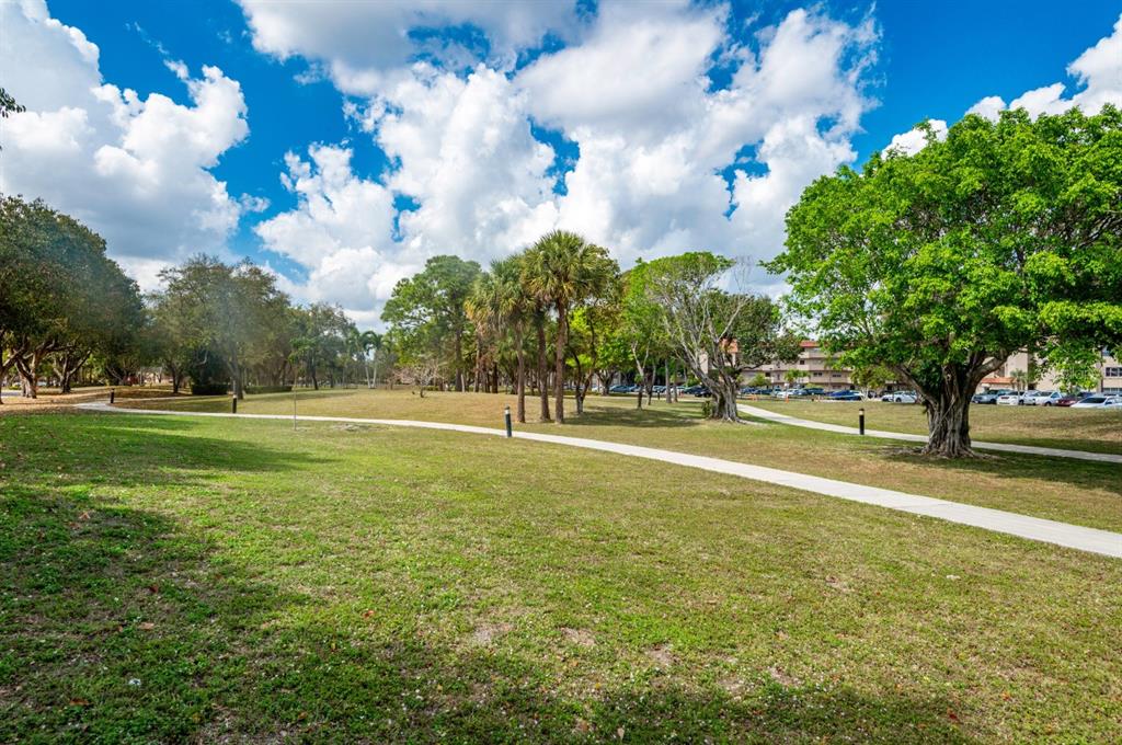 A paved walking path winds through a grassy park area with trees and palm trees — 5961 N FALLS CIRCLE DRIVE UNIT 411, LAUDERHILL, FL