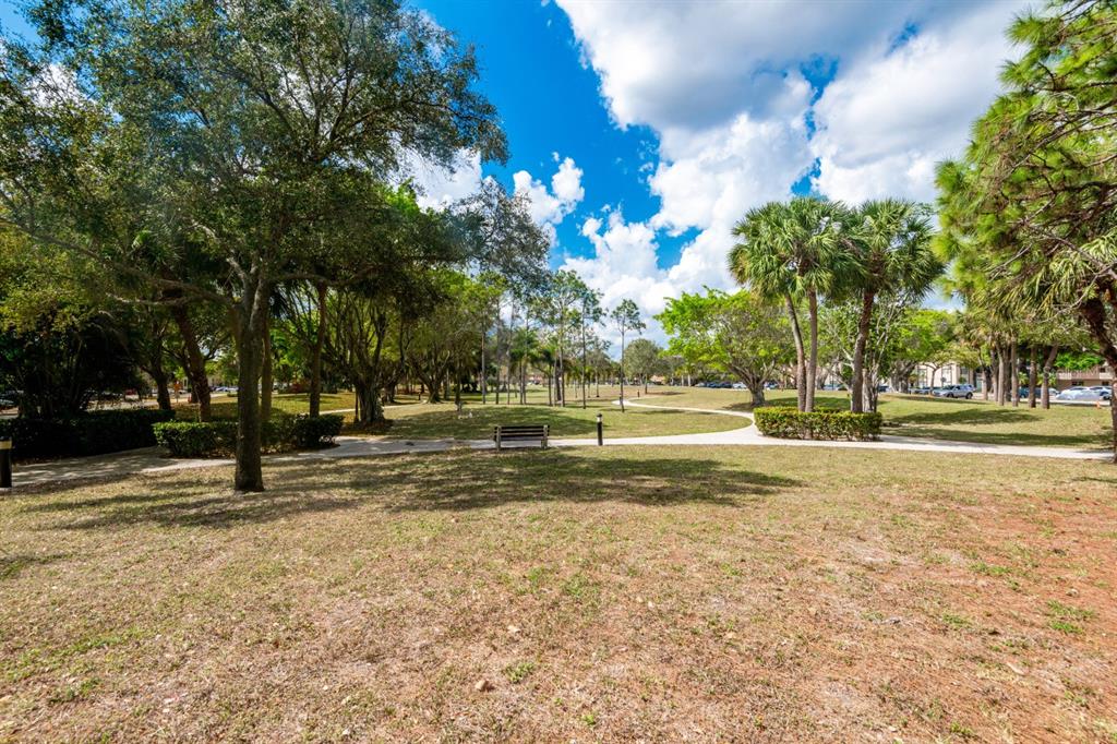 A park with a paved walking path, a wooden bench, and mature trees under clouds — 5961 N FALLS CIRCLE DRIVE UNIT 411, LAUDERHILL, FL