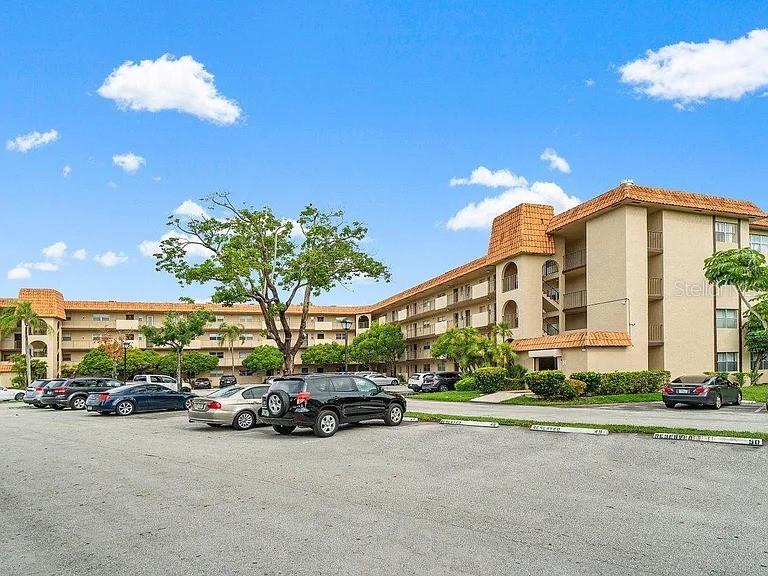 A multi-story apartment building with a parking lot in the foreground under a blue sky — 5961 N FALLS CIRCLE DRIVE UNIT 411, LAUDERHILL, FL