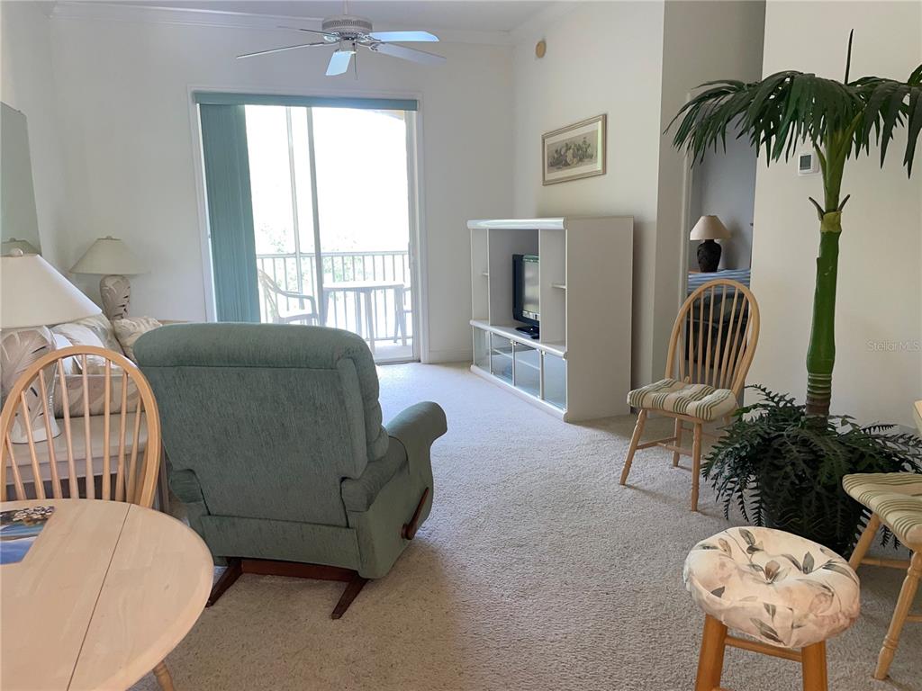 A living room features a recliner, television console, dining chairs, and a sliding glass door — 6816 DALI AVENUE UNIT 205, LAND O LAKES, FL