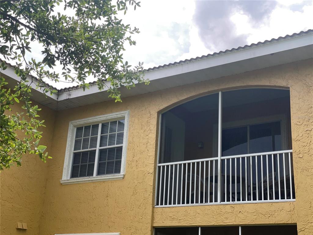 The exterior of a two-story stucco building features a screened balcony and a window — 6816 DALI AVENUE UNIT 205, LAND O LAKES, FL