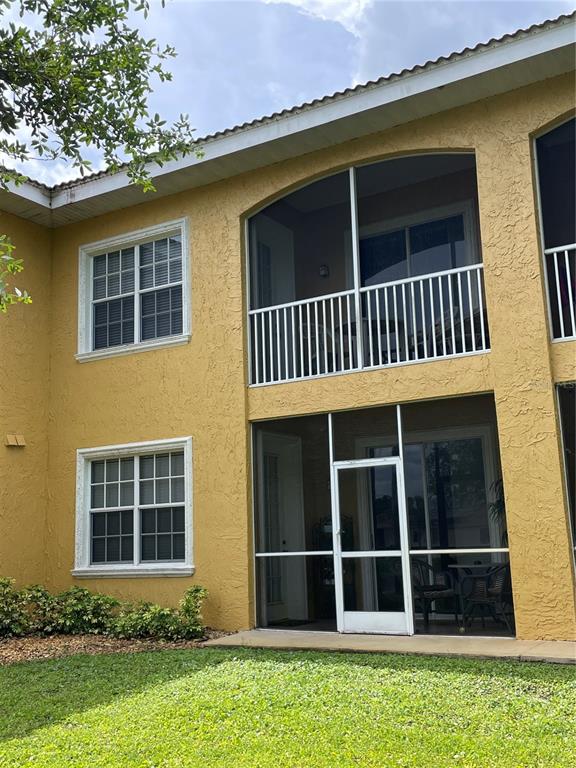 A two-story yellow stucco building features a screened-in balcony and a ground-level screened patio — 6816 DALI AVENUE UNIT 205, LAND O LAKES, FL