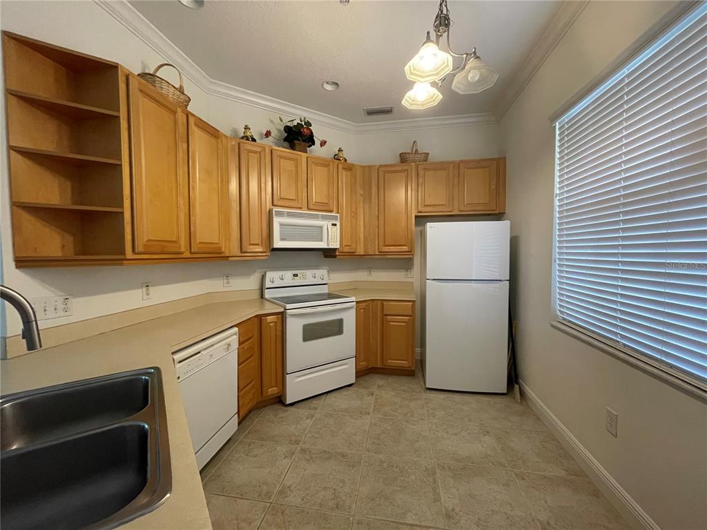 A kitchen features light wood cabinets, white appliances, beige countertops, and tile flooring — 6816 DALI AVENUE UNIT 205, LAND O LAKES, FL